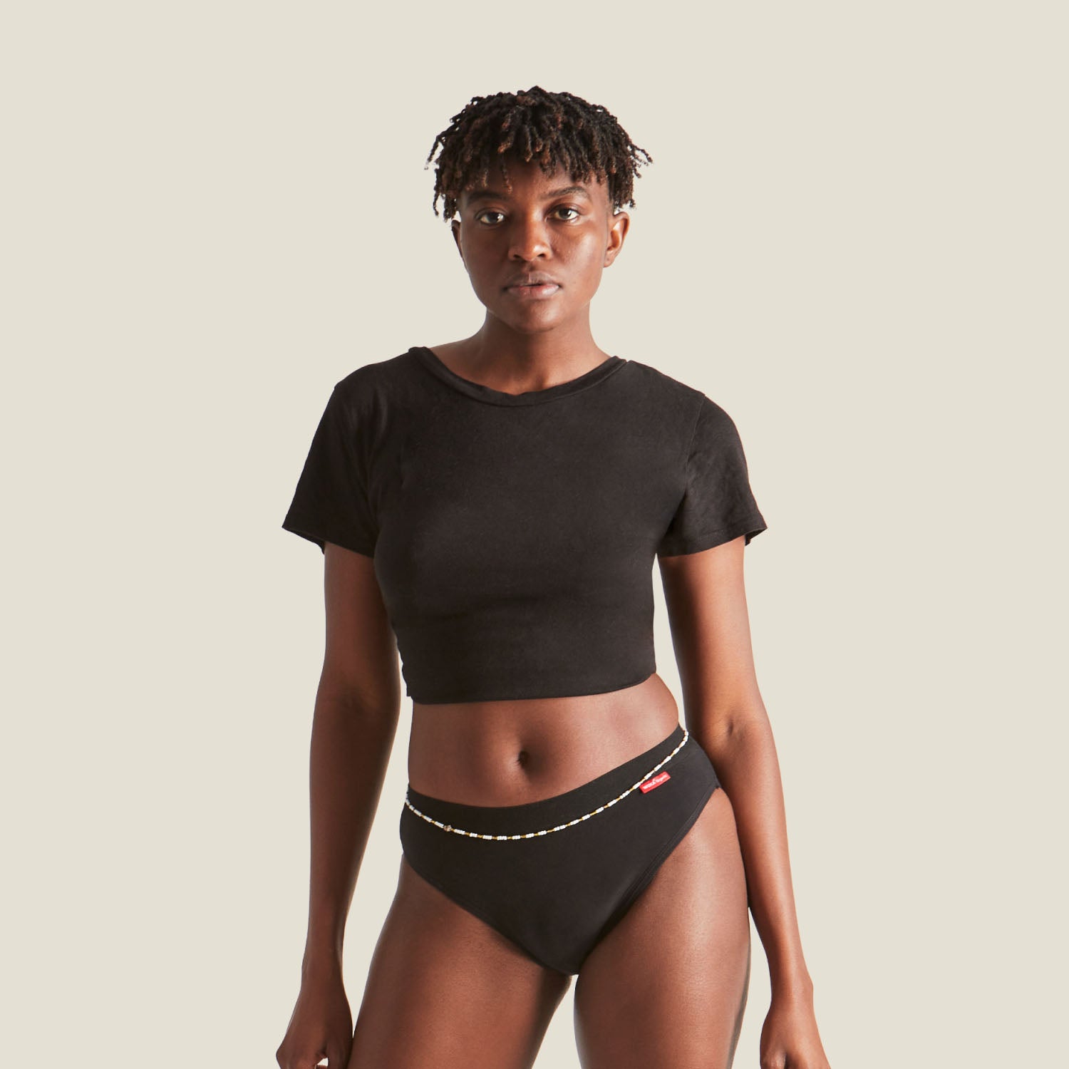 Woman wearing WUKA Ultimate™ Bikini Period Pants for medium flow, styled with a black crop top and waist beads, highlighting a comfortable and secure fit.