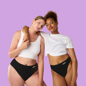Two women wearing black award-winning WUKA Stretch™ period underwear with a visible brand logo on a purple background